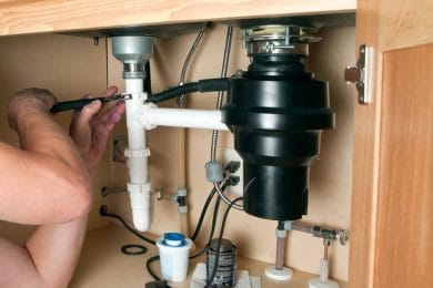 Plumber repairing a garbage disposal beneath a kitchen sink in Leesburg