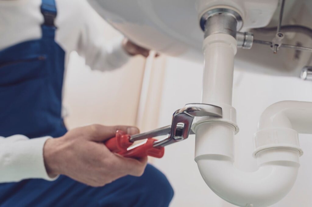 Plumber repairing a white drain pipe beneath a sink in Leesburg