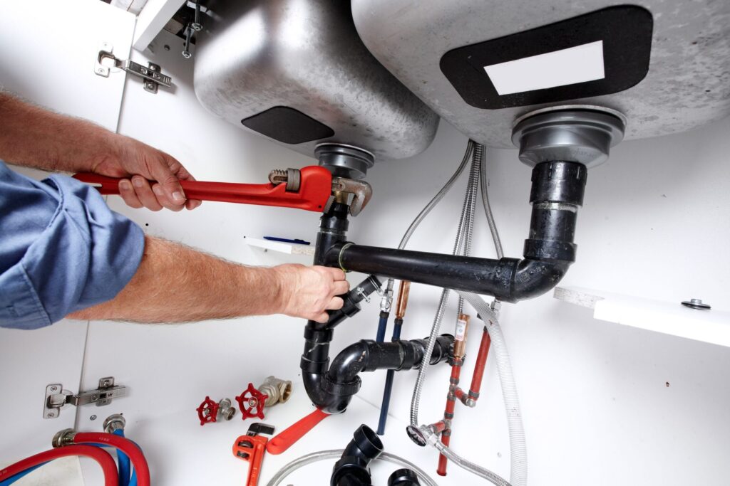 Plumber repairing drain pipes beneath a kitchen sink in Leesburg